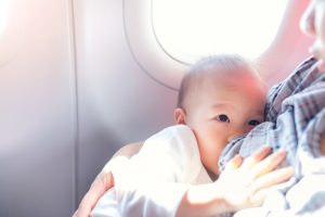 Asian mother is breastfeeding Cute little Asian 18 months toddler baby boy child on AirplaneToddler lying on mother's laps BreastFeeding in Public concept harsh sunlight overexposed at baby hand