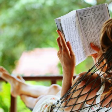 Young woman reading a book lying in a hammock