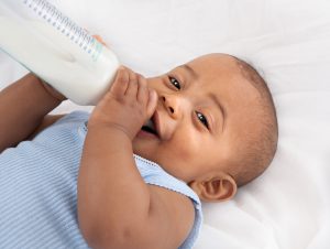 smiling 7-month old baby holding milk bottle lying down