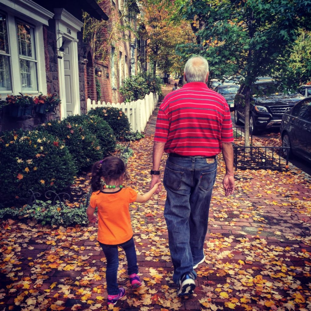 Grandpa holdings hands with granddaughter walking down sidewalk