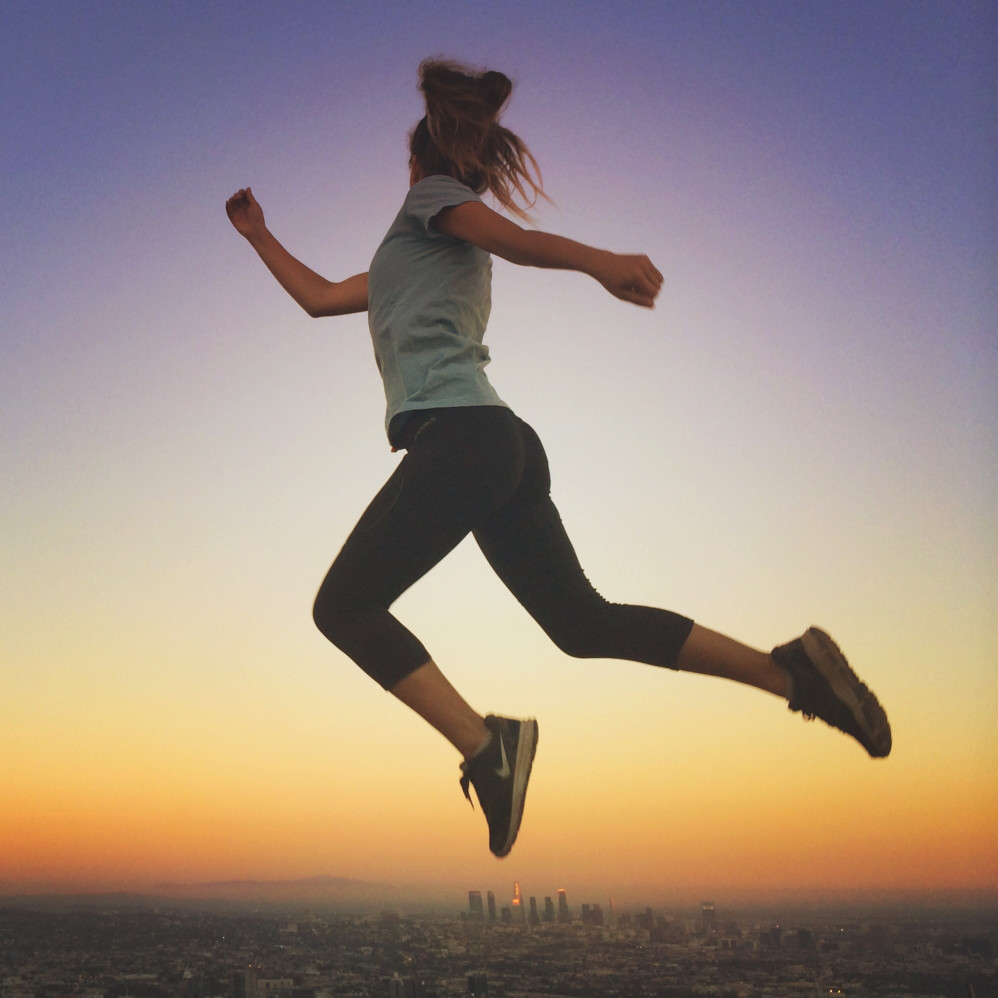 Woman jumping at sunset wearing black leggings and tennis shoes
