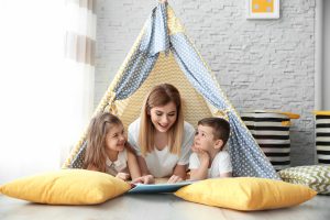 Nanny reading book to children in an indoor tent