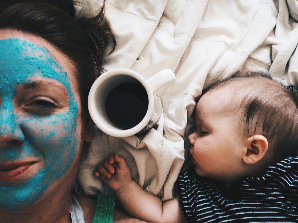 Mother wears face mask while newborn sleeps beside her