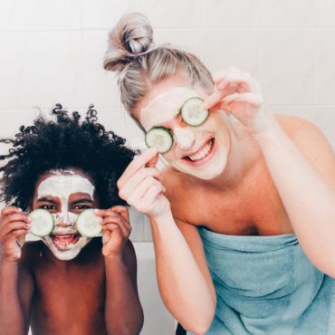 Woman and toddler smile with facemasks on holding cucumbers