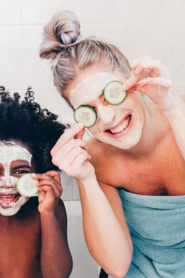 Woman and toddler smile with facemasks on holding cucumbers