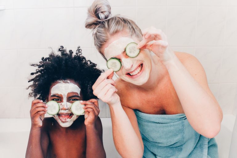 Woman and toddler smile with facemasks on holding cucumbers