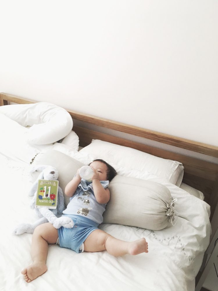 relaxed little boy lays back on bed drinking his milk
