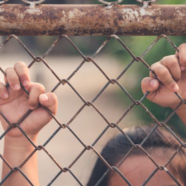 Kid holding hands behind metal fence