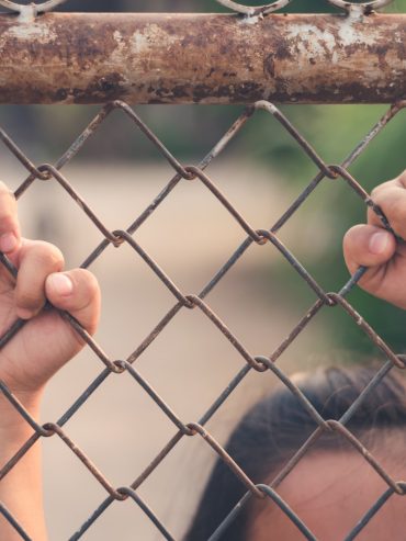 Kid holding hands behind metal fence