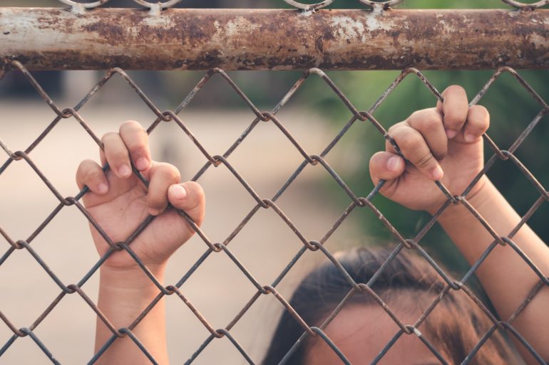 Kid holding hands behind metal fence