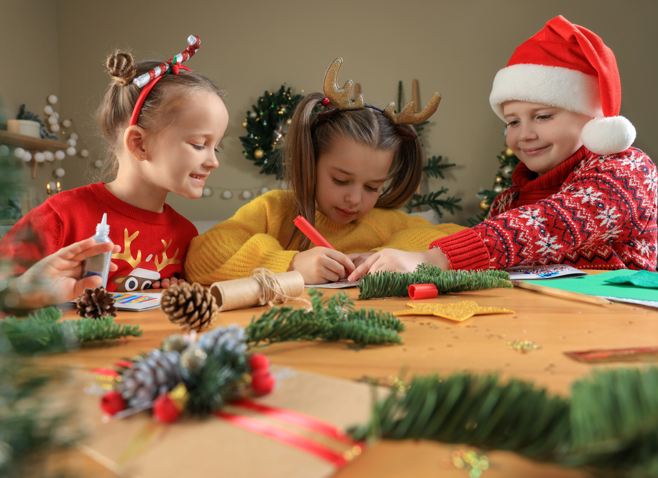 Three kids with festive sweaters making Christmas cards.