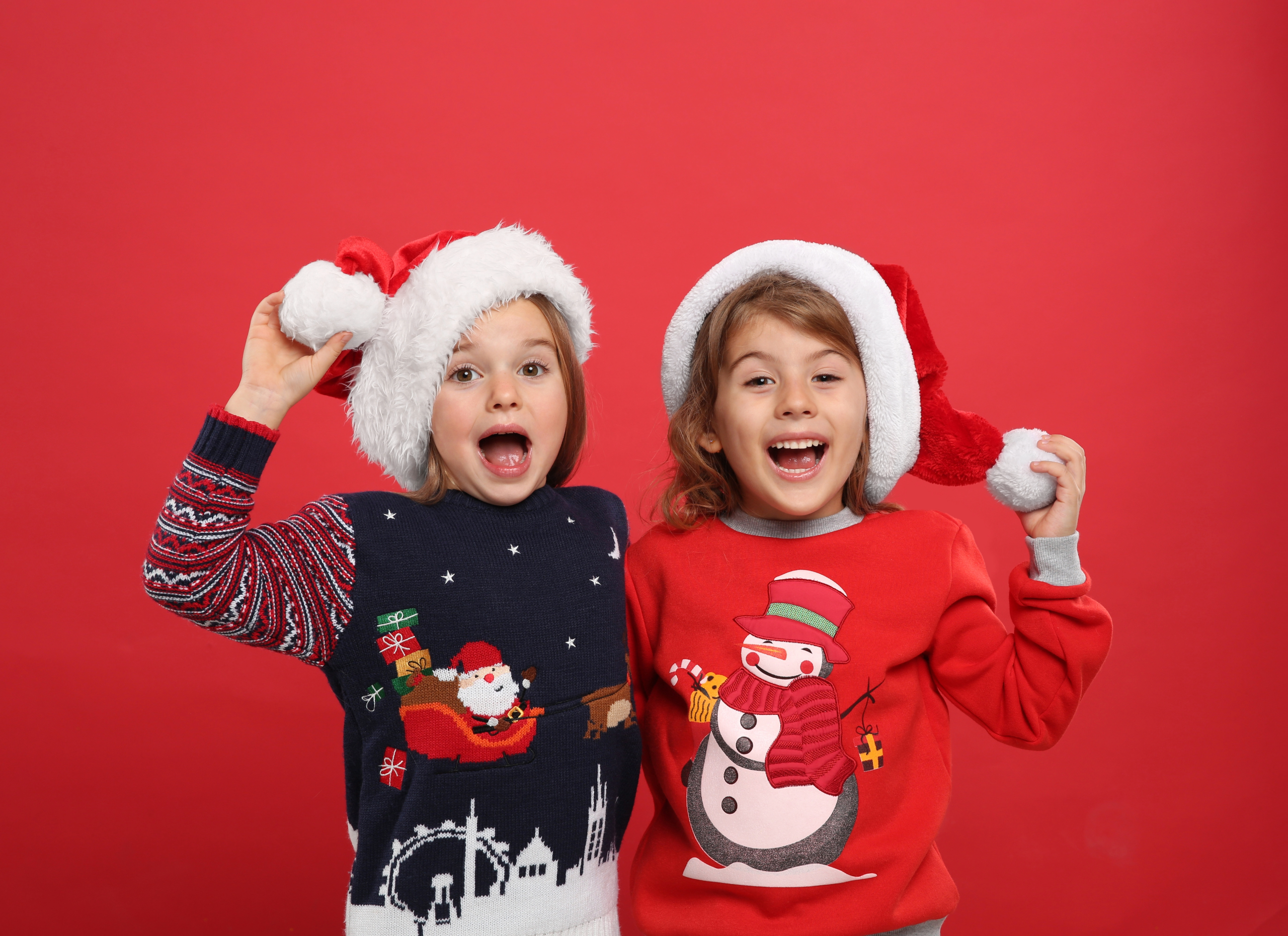 Two happy kids with Christmas hats and sweaters.