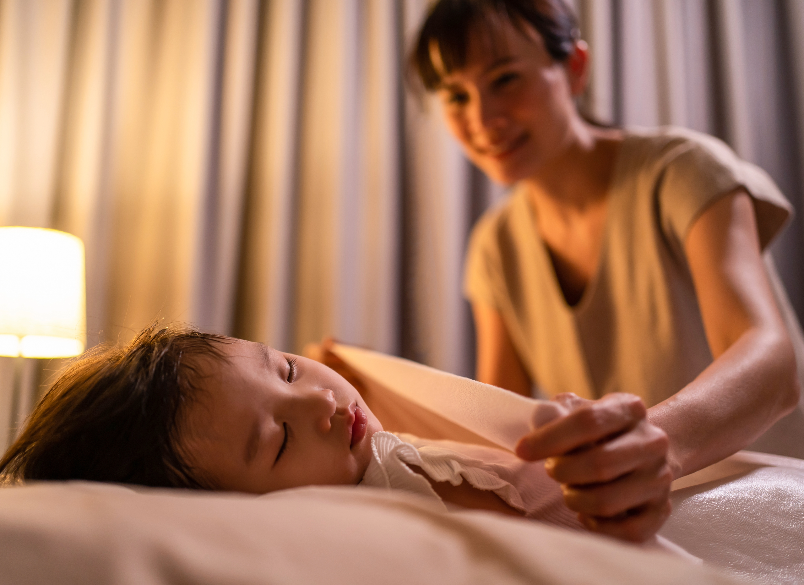 Women tucking in sleeping daughter.