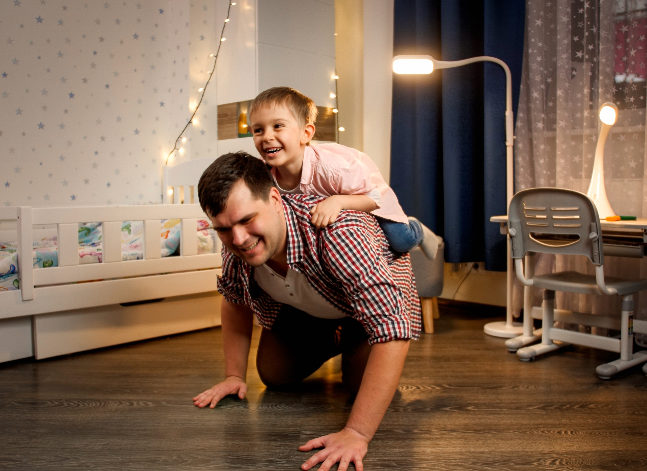 Father crawling on the floor with a child on top in the children's bedroom.