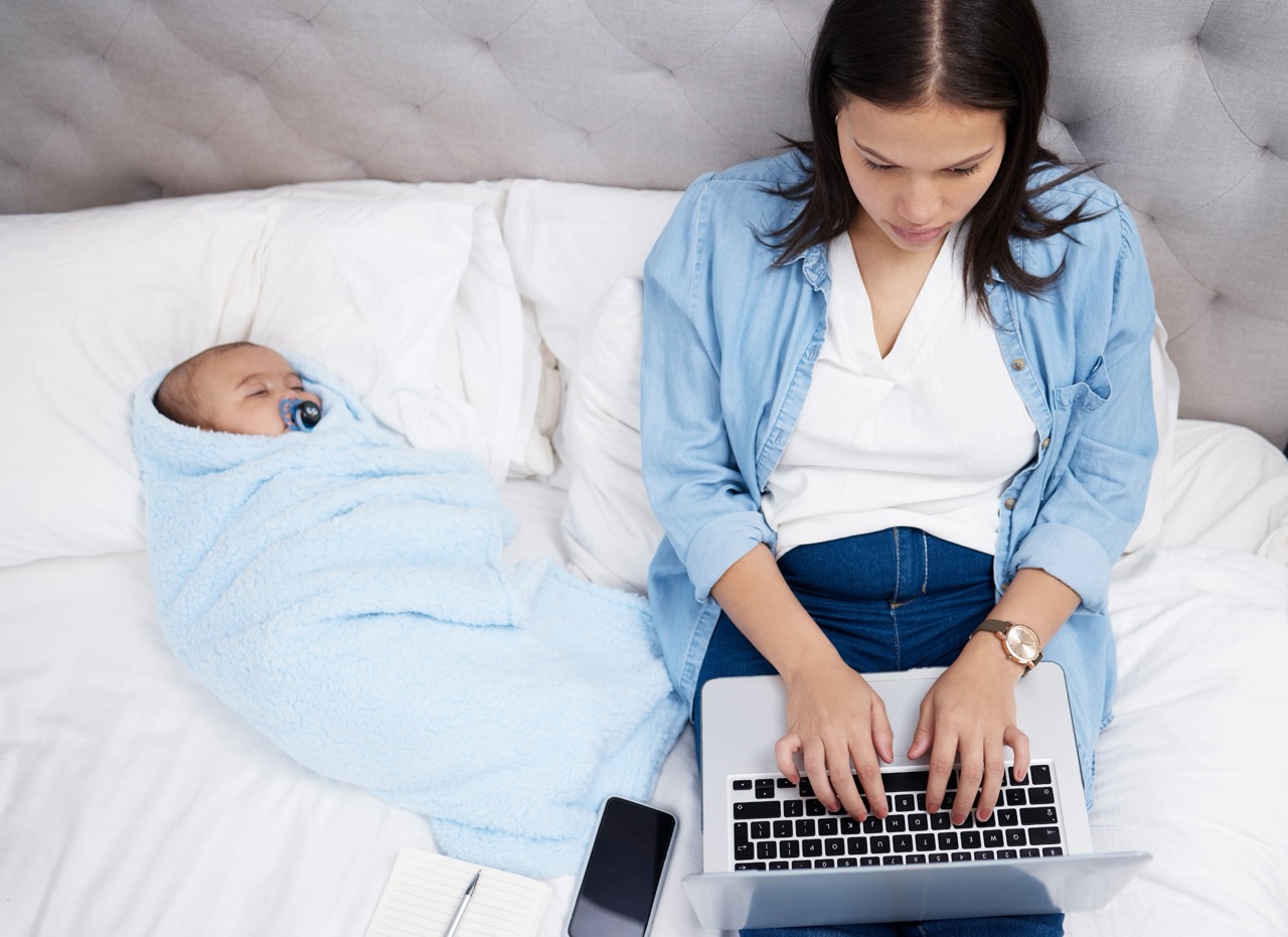 baby taking a nap in bed while mother types computer large