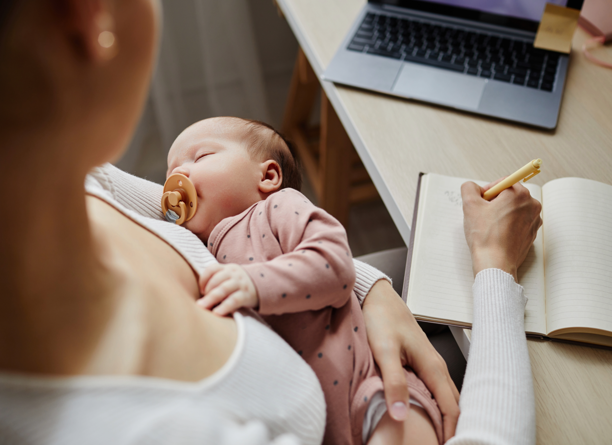 Mother making a week schedule with new born in her arm.