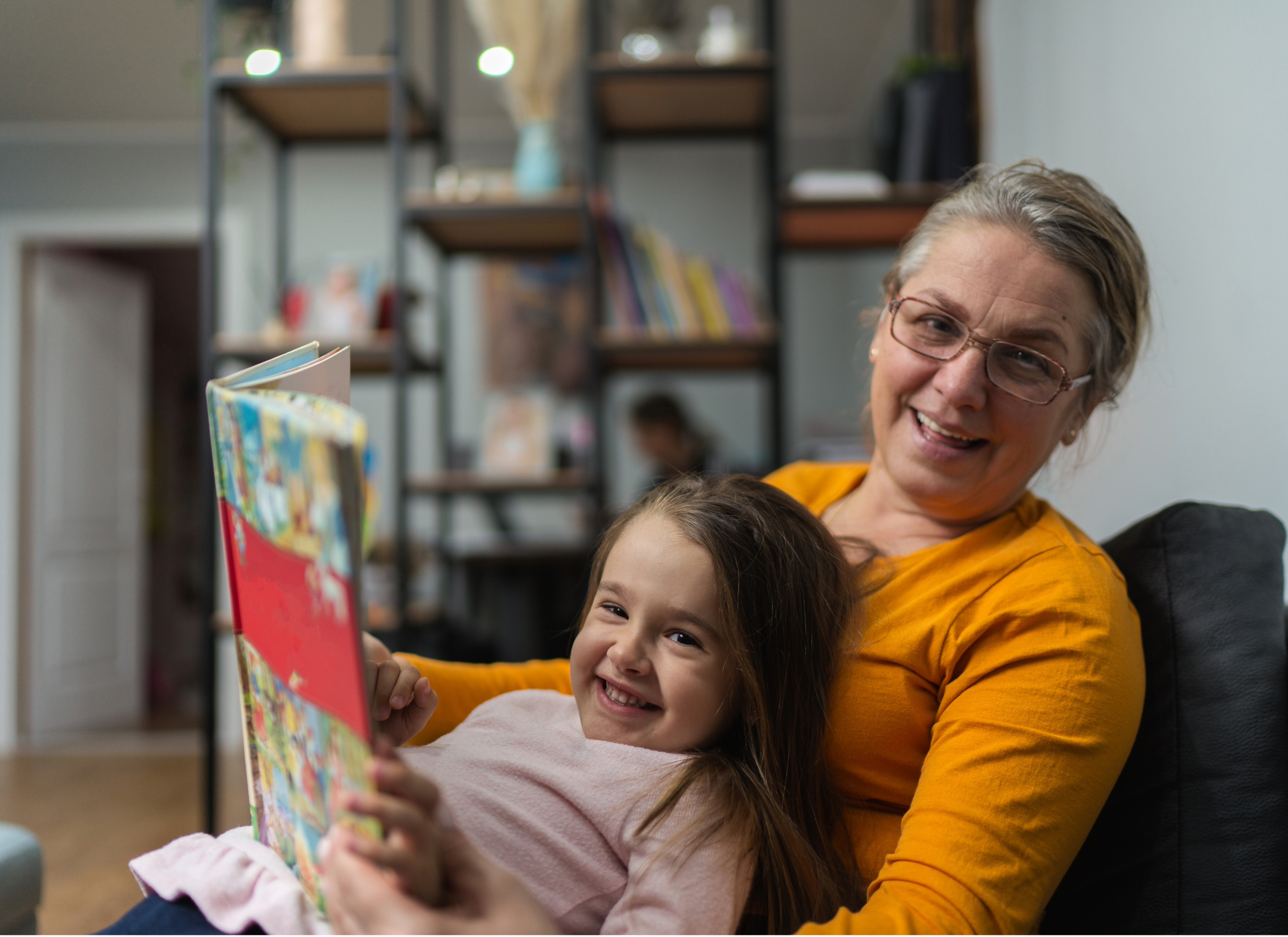 older woman reading book to kid in livingroom