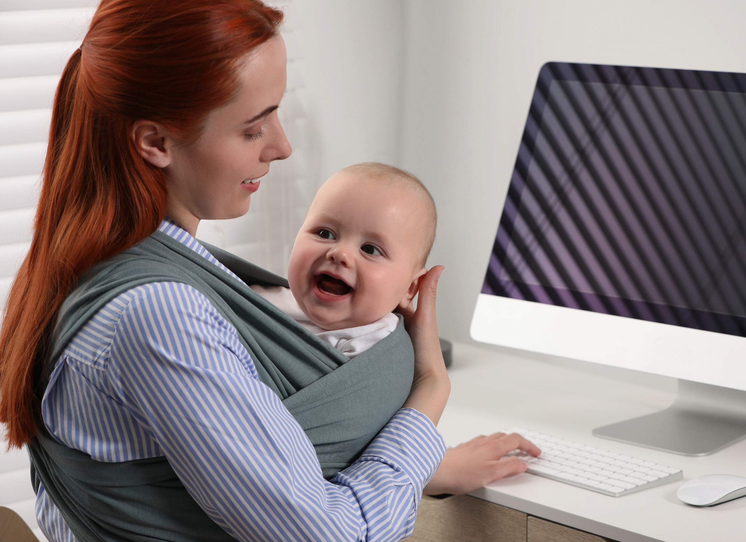 smiling baby in mother arms sitting infront of computer